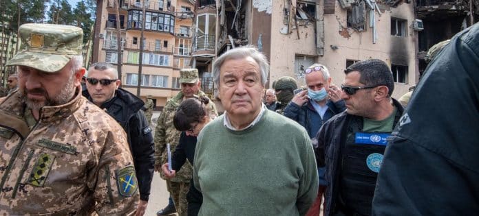 Ο Γενικός Γραμματέας του ΟΗΕ Αντόνιο Γκουτέρες σε επίσκεψή του στο Ιρπίν στην Ουκρανία τον Απρίλιο του 2022, περιτριγυρισμένος από Ουκρανούς αξιωματικούς και στελέχη του ΟΗΕ, ενώ στο βάθος διακρίνονται χαλάσματα πολυκατοικίας.