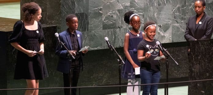 Photo of a woman and 4 children standing at the podium in the GA hall as one of them speaks © UN Photo/Eskinder Debebe