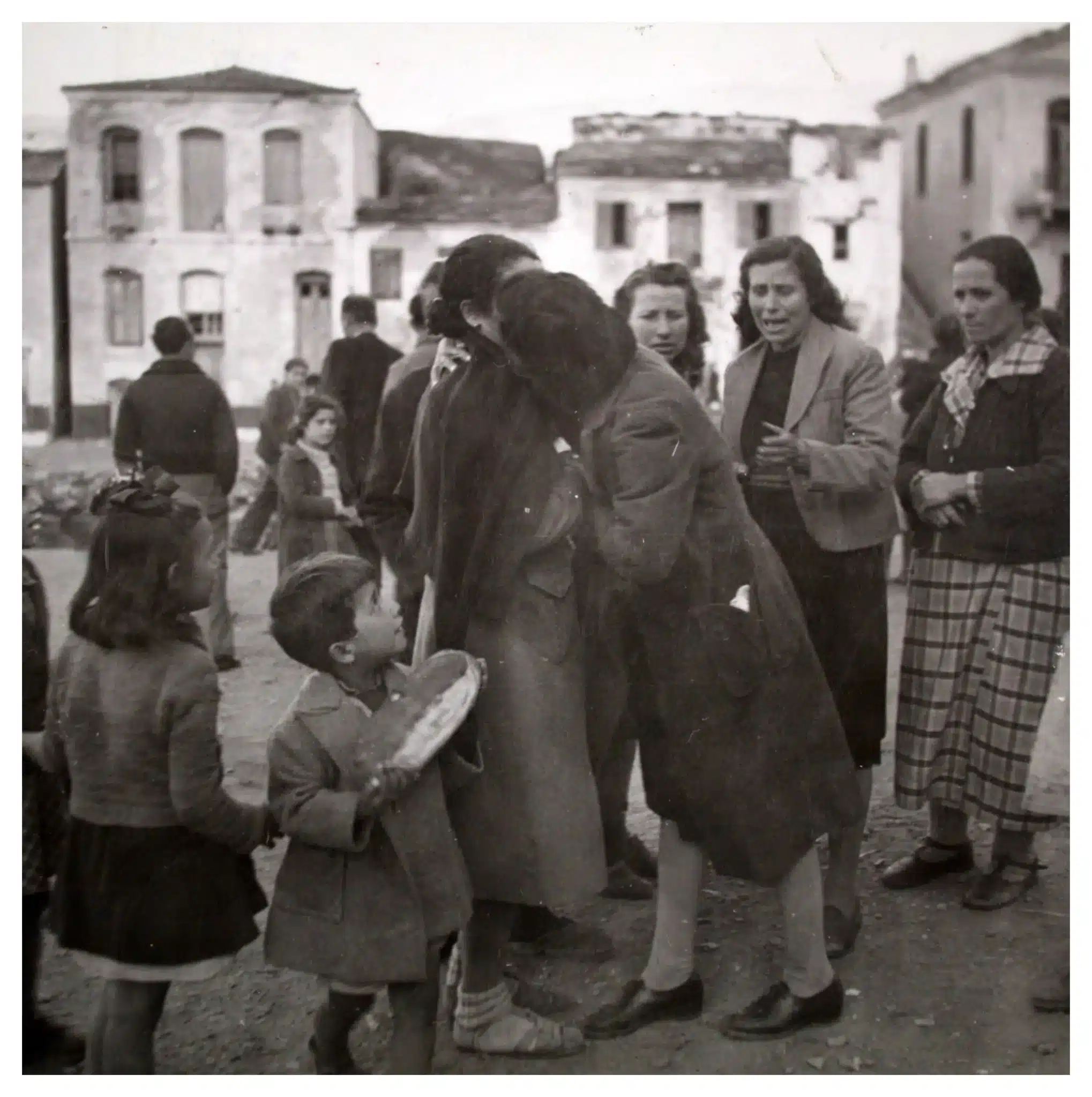 27 Γυναίκες αγκαλιάζονται και φιλιούνται συγκινημένες σε πλατεία χωριού, υπό το βλέμμα συγχωριανών τους.