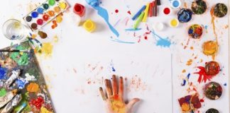 hand on white canvas surrounded by paints and brushes