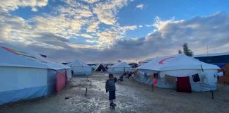 Child stands outside tents in Gaza.