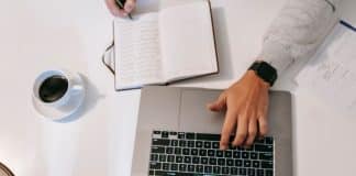 Person working on an article using a laptop and handwritten notes from a notepad
