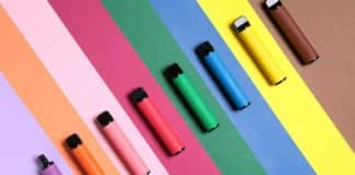 Assorted colorful electronic cigarettes and vape pens standing on a wooden surface against a dark background.