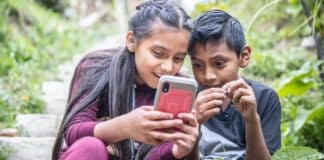 Two children sitting outside watching a phone screen