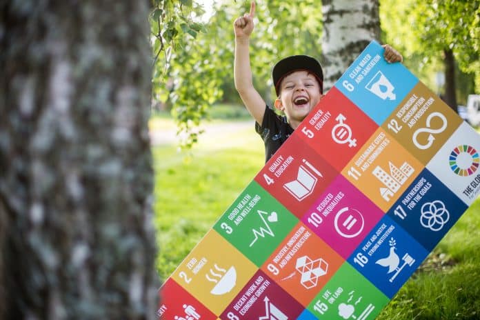 Iloinen poika joka pitää kestävän kehityksen tavoitteet kädessään