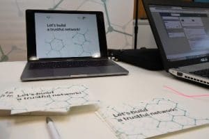 Un ordinateur et des feuilles de papier sur lesquels il est écrit 'Let's build a trustful network'