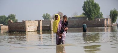 Kona með vatn upp að hnjám með barn í fangi. Mýrarkalda dafnaði eftir flóð í Sindh-héraði í Pakistan fyrr á árinu.