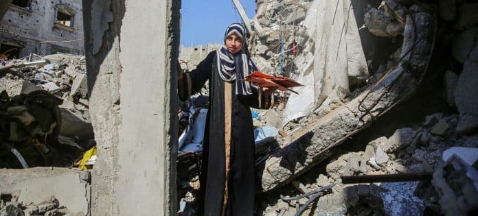Unga kona á gangi við rústir heimilis síns á Gasa. Mynd: UN Women/Suleiman Hajji