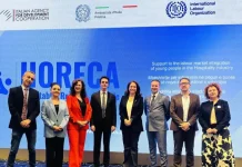 Foto di gruppo durante un evento ufficiale del progetto HORECA, con rappresentanti dell'Agenzia Italiana per la Cooperazione allo Sviluppo, dell'Ambasciata d’Italia a Pristina e dell’Organizzazione Internazionale del Lavoro, davanti a uno schermo che promuove l'integrazione dei giovani nel mercato del lavoro del settore dell’ospitalità