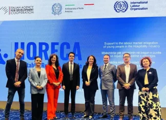Foto di gruppo durante un evento ufficiale del progetto HORECA, con rappresentanti dell'Agenzia Italiana per la Cooperazione allo Sviluppo, dell'Ambasciata d’Italia a Pristina e dell’Organizzazione Internazionale del Lavoro, davanti a uno schermo che promuove l'integrazione dei giovani nel mercato del lavoro del settore dell’ospitalità