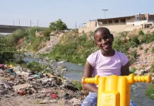 Il 16 settembre 2025 in Sudafrica, la piccola Ompfuna Nkhumeleni, di 10 anni, posa per un ritratto seduta sulla sua motocicletta di plastica accanto al fiume Juskei, inquinato.