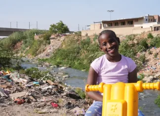 Lotta contro la povertà infantile: i progressi si arrestano a livello globale Il 16 settembre 2025 in Sudafrica, la piccola Ompfuna Nkhumeleni, di 10 anni, posa per un ritratto seduta sulla sua motocicletta di plastica accanto al fiume Juskei, inquinato.