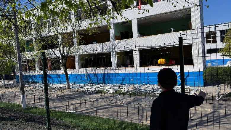 Een jongen staat naast een school die bij een aanval zwaar beschadigd raakte. Het beeld toont hoe groot het gevaar blijft voor kinderen, nu scholen in Oekraïne nog steeds onder vuur liggen. © UNOCHA/Iryna Chernysh