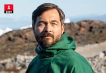 En man i grön jacka som står utomhus vid vatten