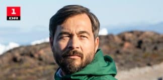 En man i grön jacka som står utomhus vid vatten