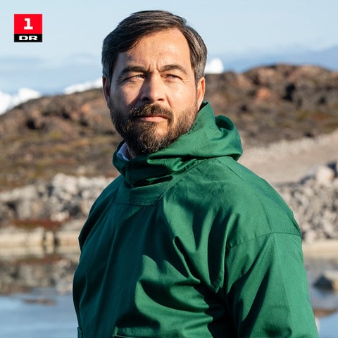 En man i grön jacka som står utomhus vid vatten