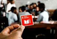 En skolklass i bakgrunden och en hand som håller upp en röd ruta med texten education