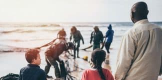En man och tre barn som håller varandra i hand framför en strand