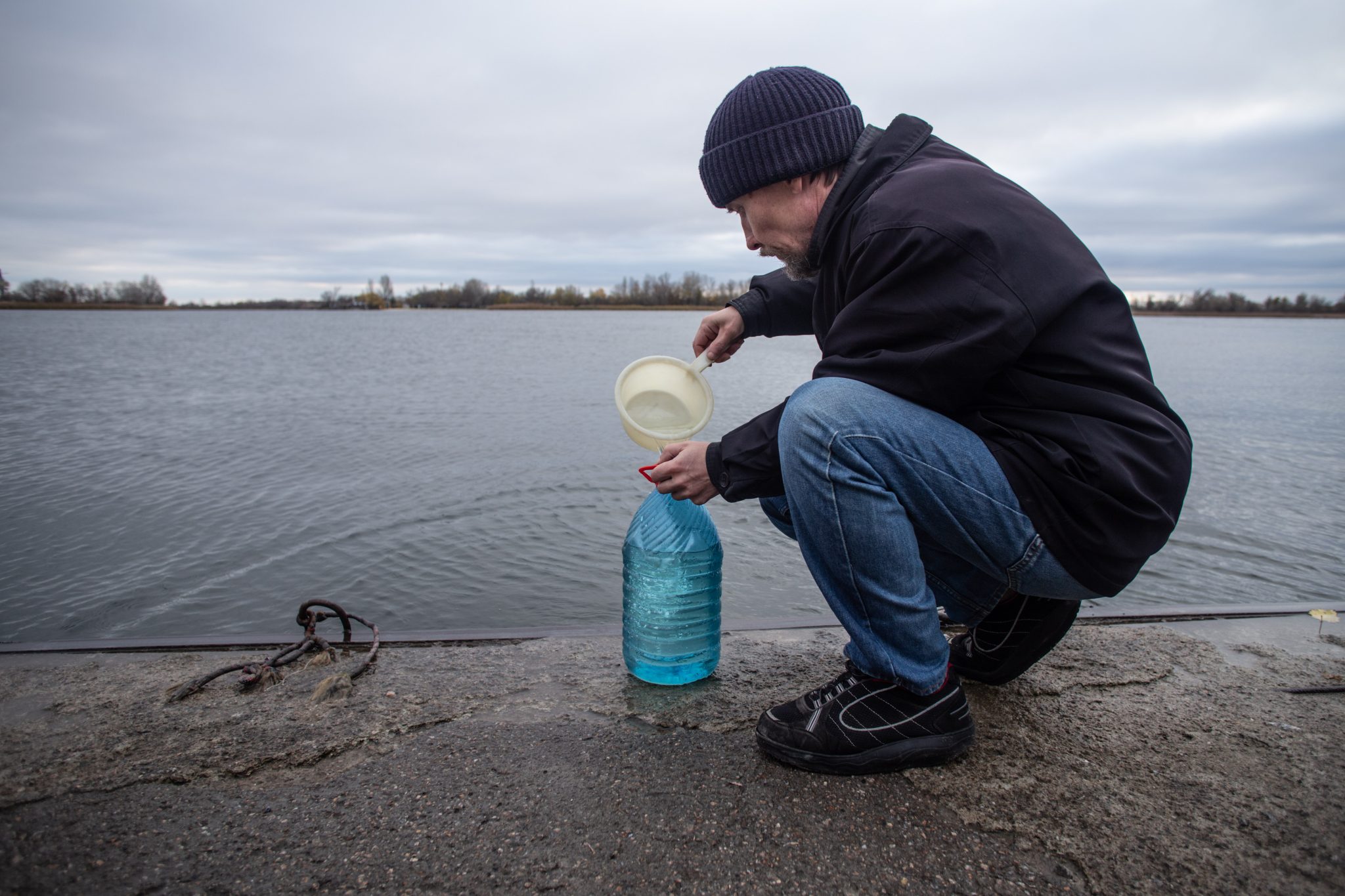 En man vid en strand som häller vatten i en flaska.