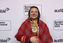 En kvinna med traditionell samisk klädsel står mot en vägg