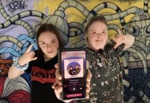 Tv[ flickor som ligger mot en färgglad bakgrund och håller upp en telefon
