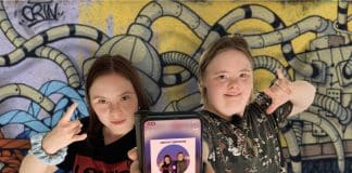 Tv[ flickor som ligger mot en färgglad bakgrund och håller upp en telefon