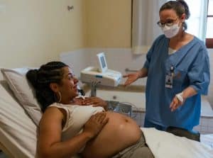 En gravid kvinna i en säng och en person som är sjukvårdspersonal